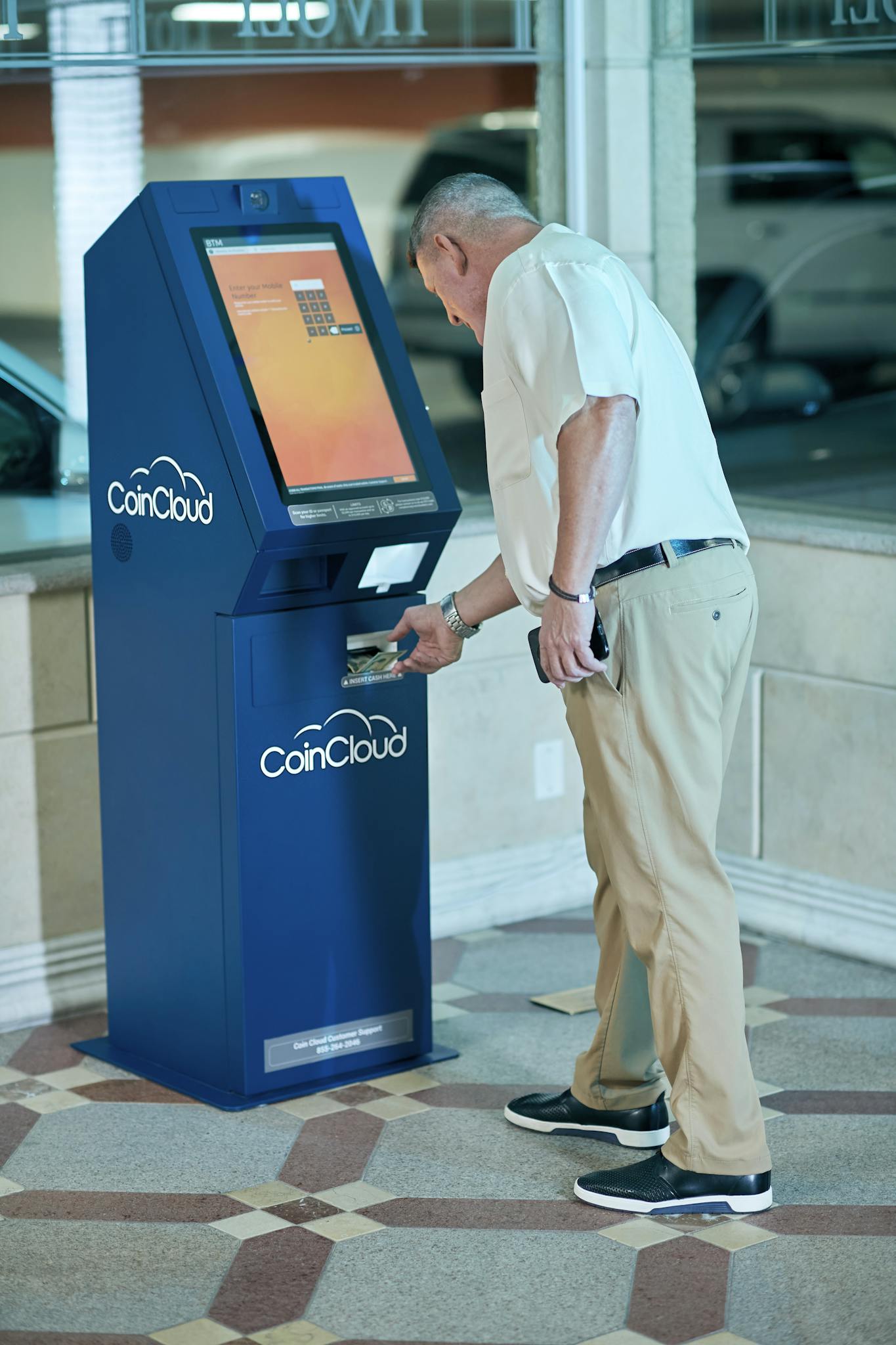 Adult man using Coin Cloud ATM for digital currency transaction indoors.